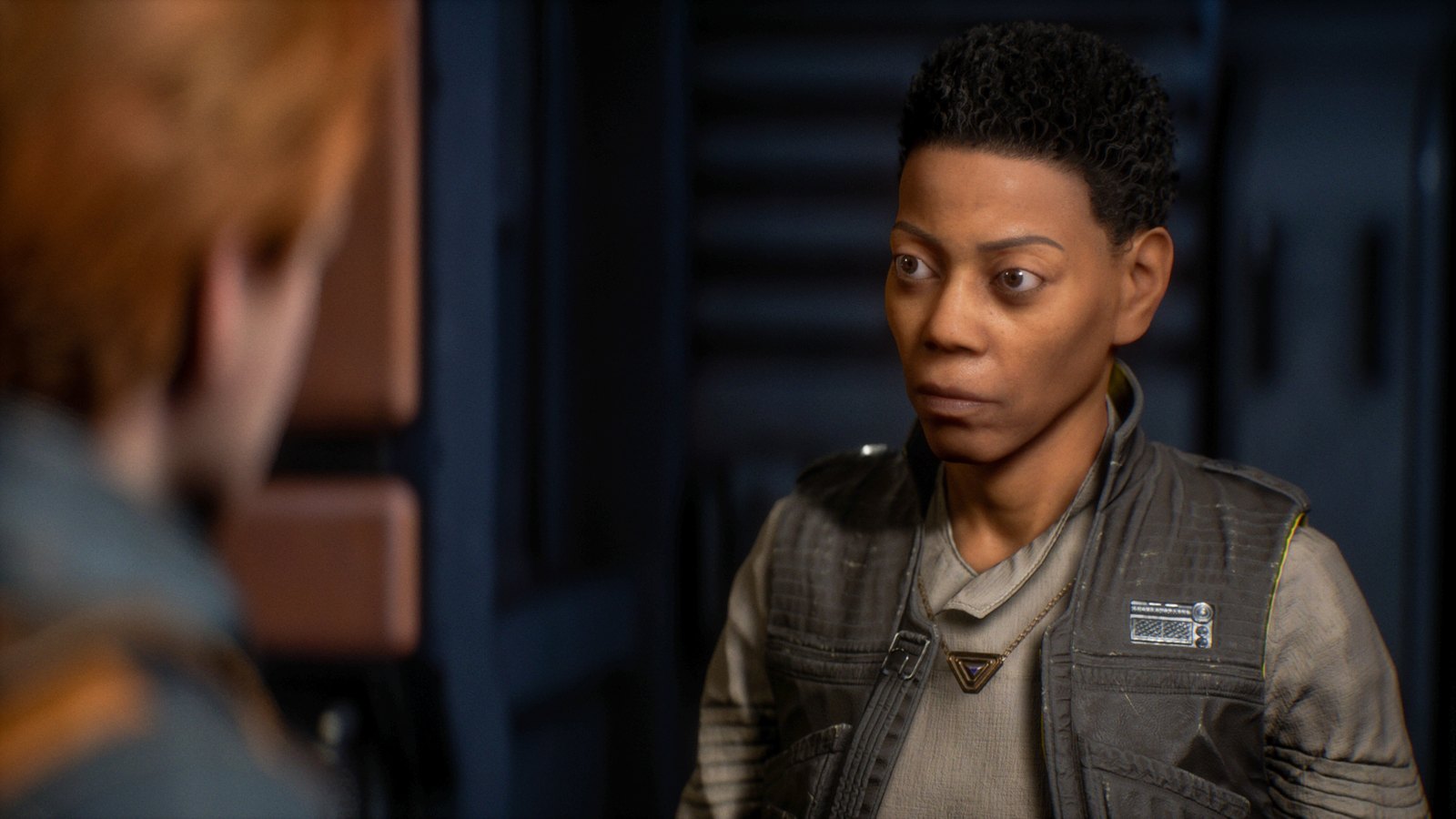 Cere Junda stands in the frame, talking to Cal, who is out of focus and facing away from the camera.