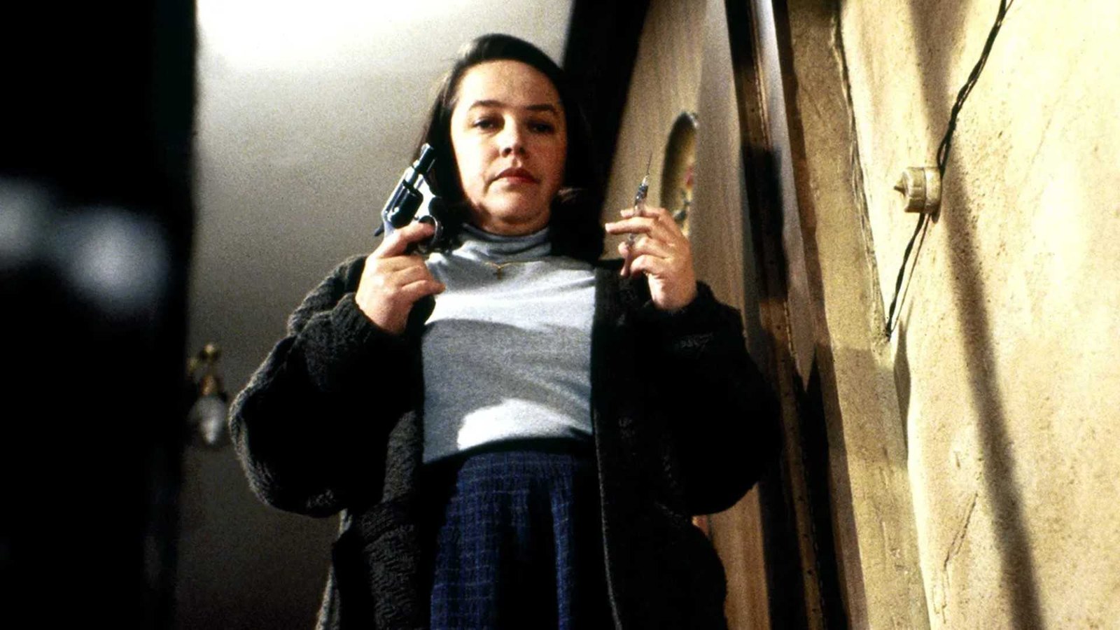 Annie (Kathy Bates) stands at the top of the stairs with a gun and needle in Misery